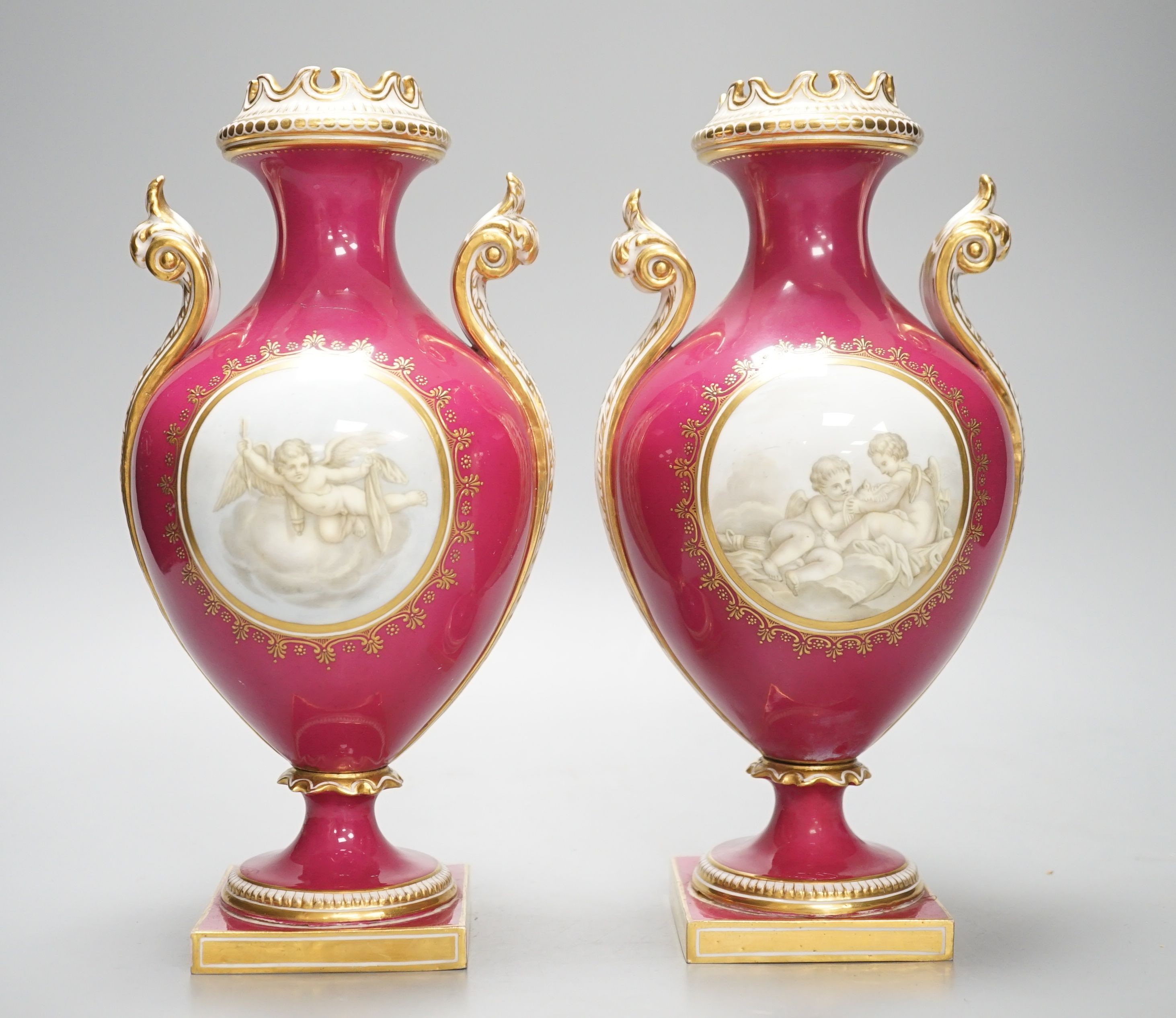 A pair of Coalport vases painted en-grisaille with cherubs in Chelsea style on a crimson ground, CSN mark in gold to one, height 23.5cm